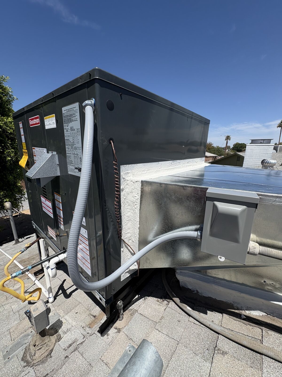 Close-up of a completed Goodman rooftop unit installation with sealed duct connections and new flex gas line