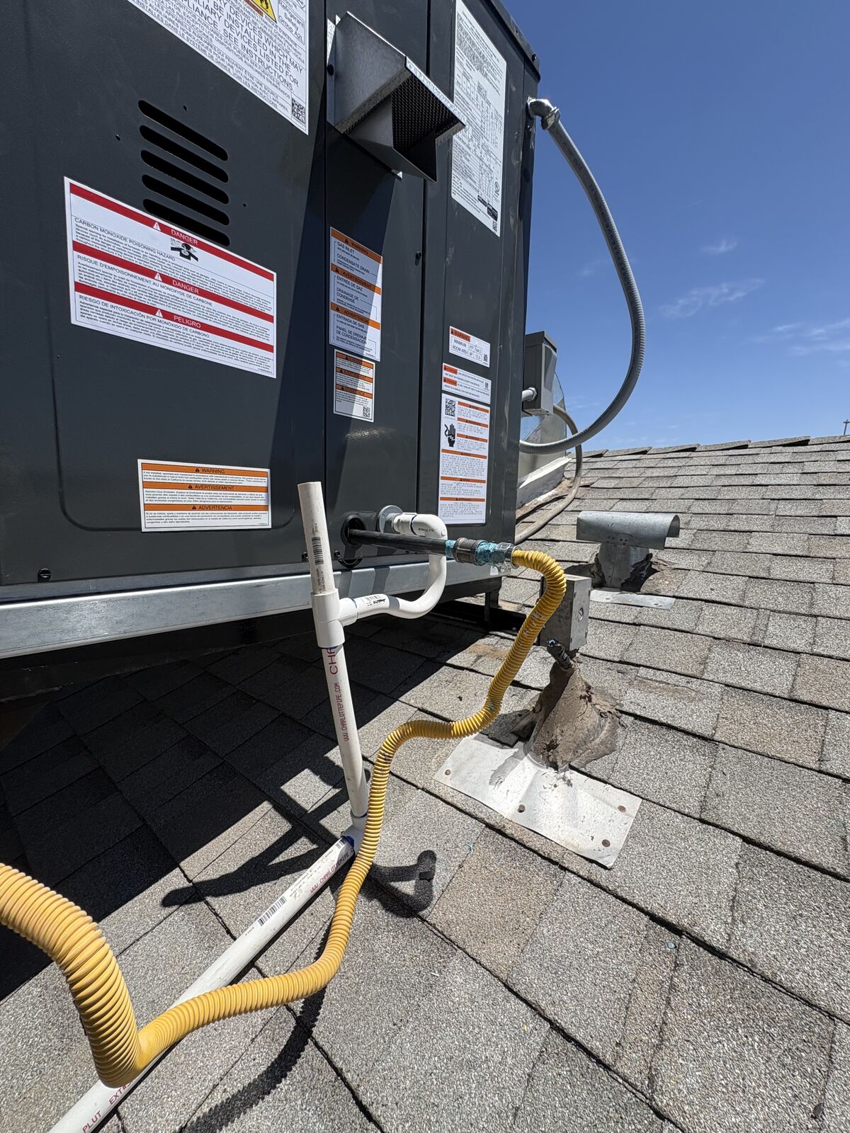 Detail of a clean gas line, condensate drain, and labeled connections on a rooftop HVAC install