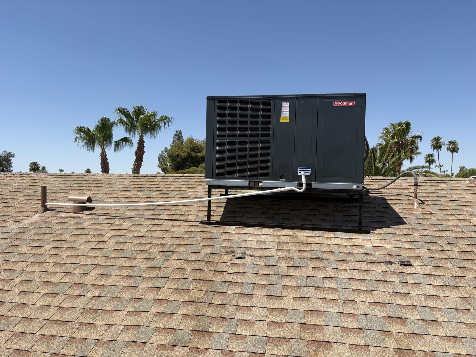 Completed Goodman rooftop package unit installation on a shingle roof in Mesa, AZ with palm trees in the background